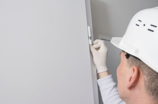 Male Construction Worker, Puts Caps On The Hinges Of The Front Door To Protect Against Dust