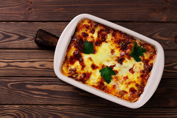Italian lasagna with meat, cheese, herbs and tomato sauce, in a baking tray, on a wooden table. Top view.