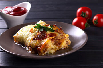 Italian lasagna with meat, cheese, herbs and tomato sauce, in a gray plate, on a wooden table.