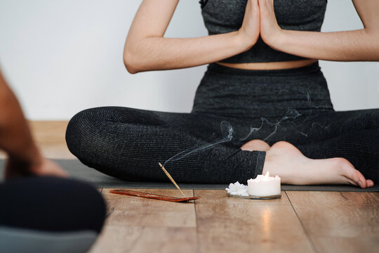 Cropped image of female instructor practicing yoga, sitting on a floor with legs closely tucked. Inhaling incense stick aroma. Meditating, relaxing, clearing consciousness. No head.