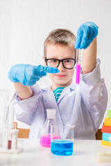 A schoolboy studies multi-colored substances in test tubes, conducts experiments - a portrait on a white background. Concept for the study of coronavirus in the laboratory