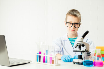 A schoolboy with a microscope examines chemicals in test tubes, conducts experiments - a portrait on a white background. Concept for the study of coronavirus in the laboratory