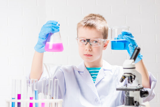 A schoolboy with a microscope examines chemicals in test tubes, conducts experiments - a portrait on a white background. Concept for the study of coronavirus in the laboratory
