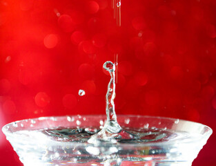 Close-up of water drop falling into a glass on red background