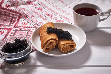 Pancakes with black caviar on a white wooden background. A traditional treat for Shrove Tuesday.