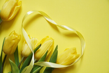 Five yellow tulips on a yellow background with yellow heart made of ribbon