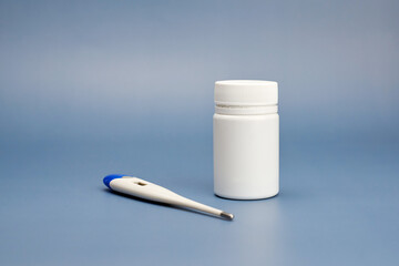 Jar of pills and electronic thermometer on a blue background.