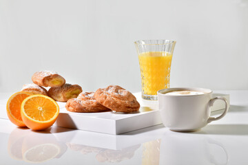 Traditional sweet pastries surrounded by a coffee cup, orange juice and an orange cut in half on a table. Traditional breakfast concept.
