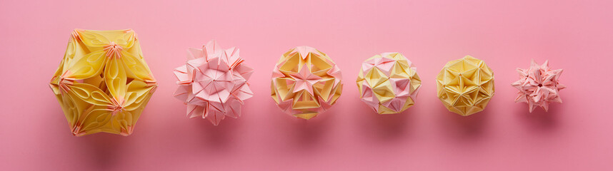 Fototapeta premium Set of multicolor handmade modular origami balls or Kusudama Isolated on pink background. Visual art, geometry, art of paper folding, paper crafts. Top view, close up, selective focus, copy space.