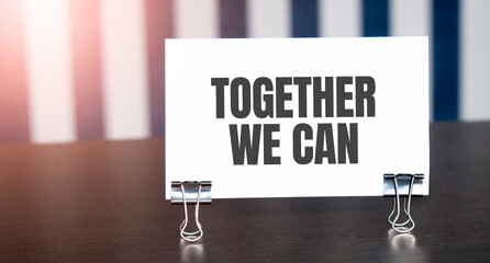 Together We Can sign on paper on dark desk in sunlight. Blue and white background