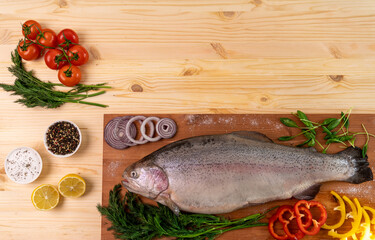 fresh trout on a natural wooden board decorated with fresh vegetables. view from above. place for your inscription.