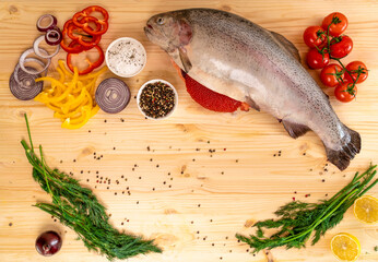 fresh trout with a cut belly from which red caviar falls out lies on a natural wood countertop decorated with vegetables and herbs