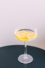 Cocktail with martini and two orange slices. Trendy champagne glass on black table and gray wall.