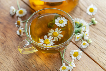 Fototapeta na wymiar Herbal chamomile tea and chamomile flowers near teapot and tea glass on wooden table. Countryside background.