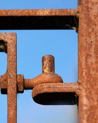 Close-up of old rusty wrought iron gate hinge seen against a blue sky