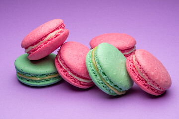 Fototapeta na wymiar Colorful sweet macarons or macaroons, flavored cookies on purple background.