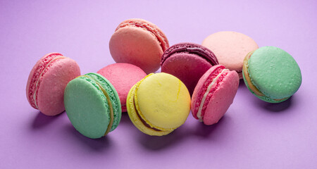 Colorful sweet macarons or macaroons, flavored cookies on purple background.