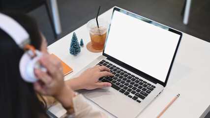 Young woman wearing headphone and working with computer laptop while sitting in modern coffee shop.