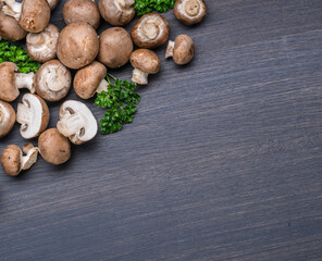Brown colored edible mushrooms or cremini mushrooms on black table with herbs. Top view.