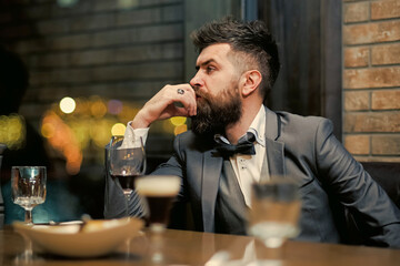 Confident man sitting at bar. Guy in cafe rest with wine glass. Businessman with long beard drink in bar.