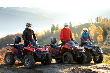 Happy drivers in protective helmets enjoying extreme riding on ATV quad motorbikes in summer...