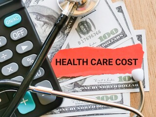 Phrase HEALTH CARE COST written on strip paper with stethoscope,calculator and fake money. Medical and health concept.