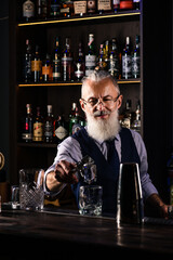 Barman making a cocktail and putting a large ice cube into the glass on the bar counter