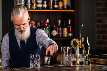 Barman making a cocktail and putting a large ice cube into the glass on the bar counter