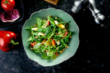 Mix salad with persimmon, mozzarella, spinach and nuts, served in a green bowl on a dark marble background. Veggie salad. Restaurant food