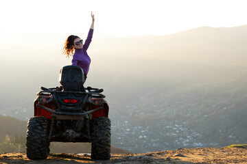 Young happy woman enjoying extreme ride on atv quad motorbike in autumn mountains at sunset.
