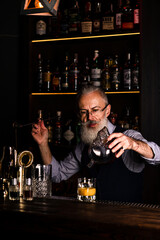 gray-haired man with a beard bartender prepares a cocktail