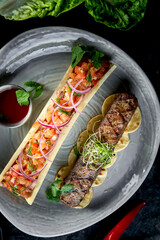 Appetizing Turkish lamb lula kebab with tomato tartare and red sauce, served in a gray plate. Dark marble background. Barbecue meat, restaurant food.