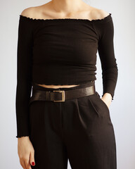 Young woman wearing all black outfit with off shoulder top and black high-waisted trousers isolated on white background.