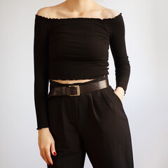 Young woman wearing all black outfit with off shoulder top and black high-waisted trousers isolated on white background.