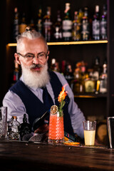 Stylish brutal barman makes a cocktail at bar counter background