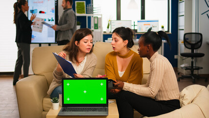 International business team talking to african woman discussing company plan with mockup laptop in front of camera. Leader explainig project strategy using green screen pc with chroma key display.