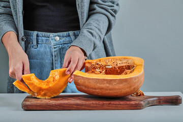 A woman hand cutting a slice of pumpkin with knife on the wooden board