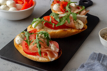 Bruschetta with ham, mozzarella, tomatoes and arugula. Wine appetizer. Snack.