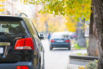 Fototapeta premium Cars parked in a row on a city street side on bright autumn day.