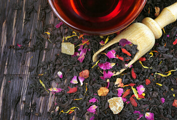 black blended tea with flower petals and dried fruit on a wooden scoop. top view
