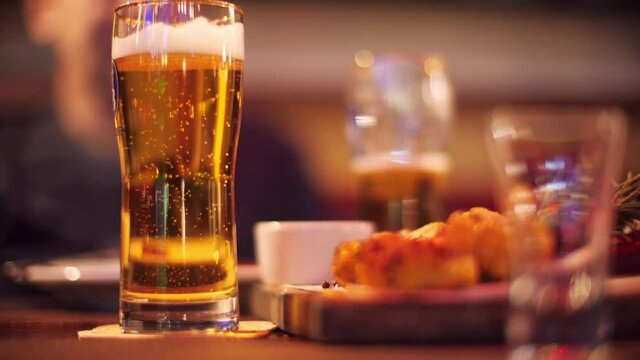 Beer bubbles in glass on table in pub with snacks on background unrecognizable talking person. Cold beer glass with bubbles and foam in cafe