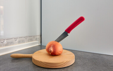 A wide-angle shot of a knife in an onion on a wooden cutting board