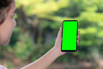 Happy Teenage woman using mobile phone app, playing game, relax on green bokeh background. Green screen smart phone for graphic display montage.