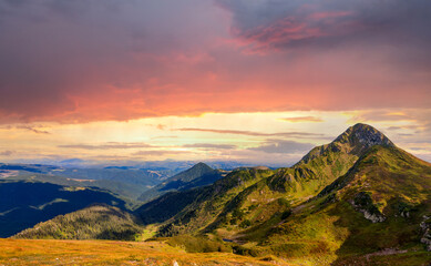 Naklejka na ściany i meble Sunset landscape of high mountain peaks under vibrant colorful evening sky.