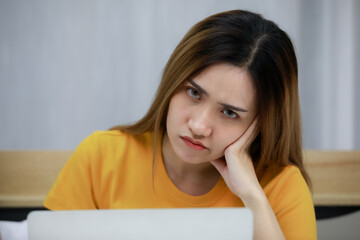 Angry bored. Asian beautiful woman wearing a Orange dress is working online on the bed in the bedroom at home. Concept Angry bore woman Not satisfied.