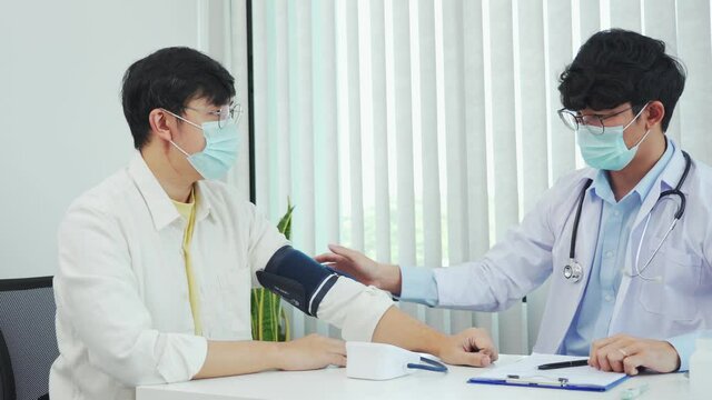 Asian doctor is using a patient's blood pressure monitor at the time of his annual check-up and explains his blood pressure.
