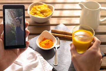 Selective focus on an energetic breakfast of Indian golden milk cereal with turmeric and cinnamon while watching a boy stretching and exercising on his cell phone.
