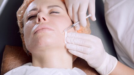 Cosmetologist making treatment procedure to patient. Beautician makes injections in the woman’s face. Mesotherapy. Doctor's hands in white medical gloves put injections in female face.