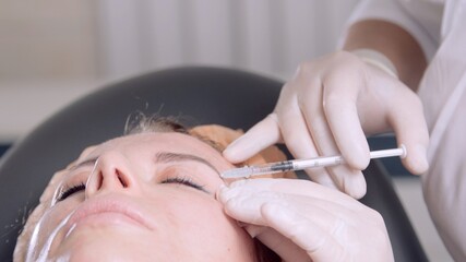 Obraz na płótnie Canvas Doctor's hands makes injections into female eyebrow. Mesotherapy treatment in the beauty salon. Beautician in gloves put injections in the face. Cosmetologist making treatment procedure to the patient
