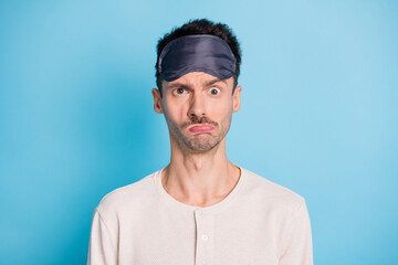 Portrait of funky disappointed guy wearing eye sleep mask grimacing isolated over bright blue color background